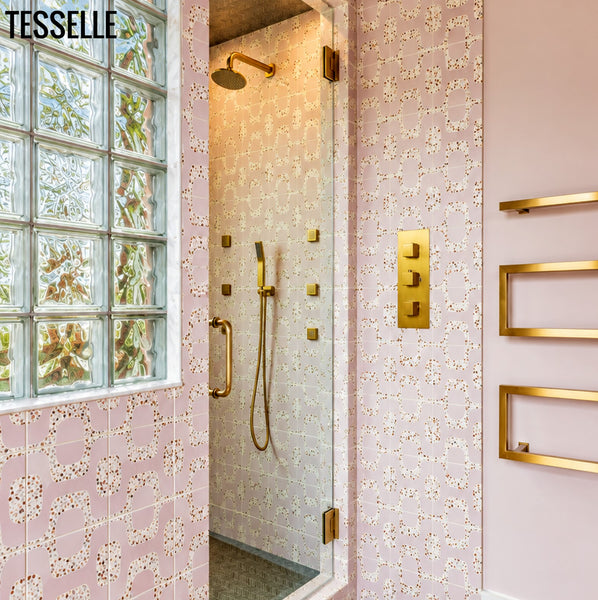 A luxury bathroom interior featuring a glass shower door with a gold shower fixture, set against Ipanema Rosa Terrazzo tiles